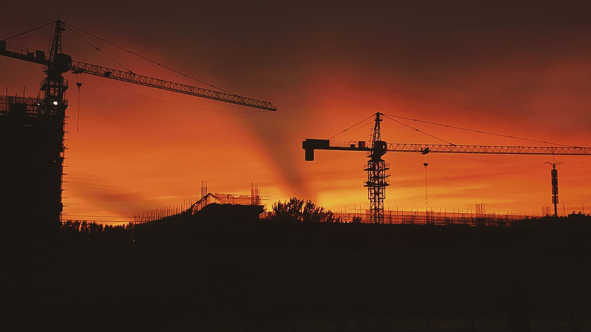 Tower cranes silhouetted against a golden-hour sky at a high-rise construction site